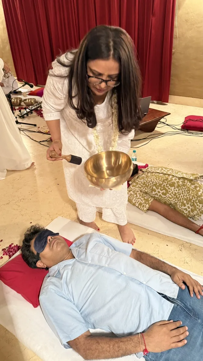 Pooja holding a singing bowl over a resting client