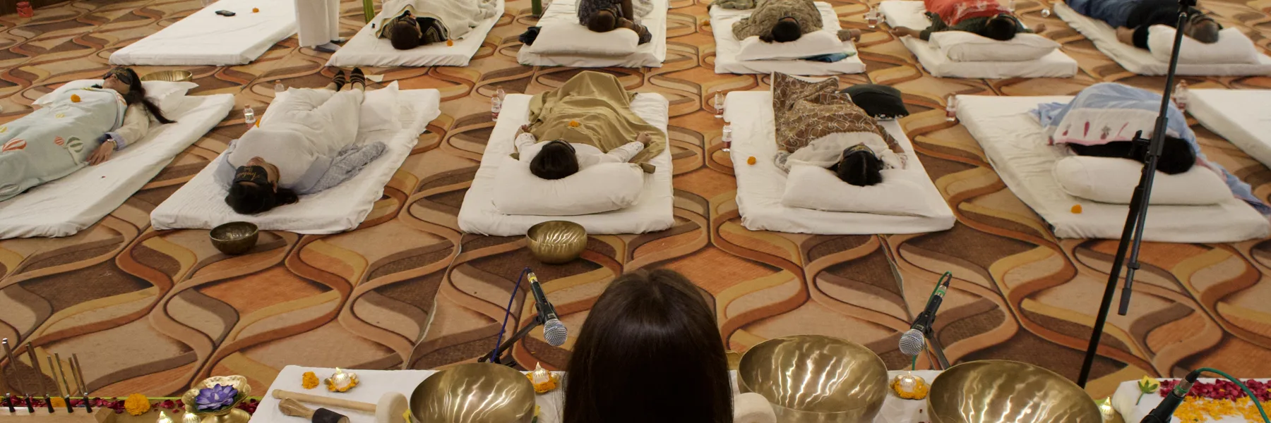 A group sound bath with singing bowls and guests resting on mats